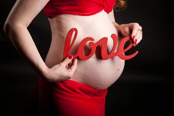 Belly of a pregnant woman in red dress,mother hand with the word love — Stock Photo, Image