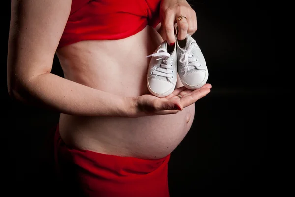 Ventre d'une femme enceinte, les mains de la mère tenant des chaussons roses bébé, fille nouveau-né — Photo