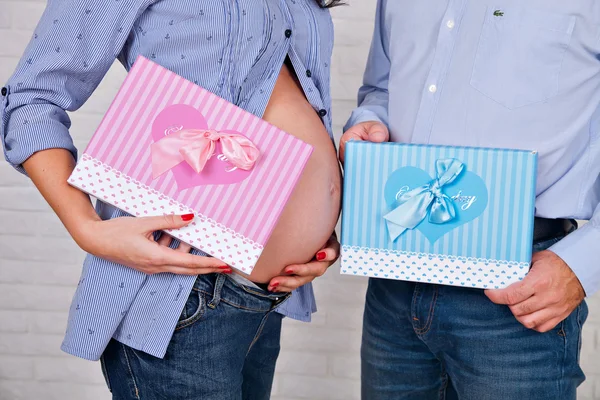 Νεαρή οικογένεια περιμένει μωρό, η χέρια ο πατέρας και η μητέρα, κρατήστε παρατεταμένα πατημένο ένα ροζ και μπλε κουτιά με δώρα, νεογέννητο αγόρι ή κορίτσι — Φωτογραφία Αρχείου
