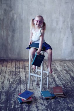 Kitaplı, gözlüklü, gülümseyen küçük kız.