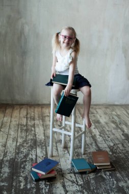 Kitaplı, gözlüklü, gülümseyen küçük kız.