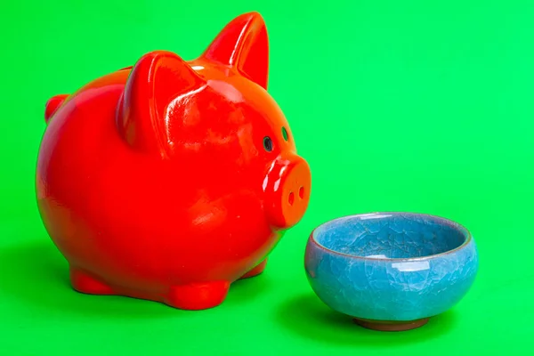 red pig piggy bank in front of an empty  bowl on a green background