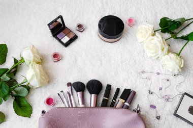 top view of the working area notebook with pen and decorative cosmetics for makeup, soft brushes and flowers, beautiful background closeup