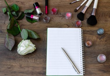 top view of the working area notebook with pen and decorative cosmetics for makeup, soft brushes and flowers, beautiful background closeup