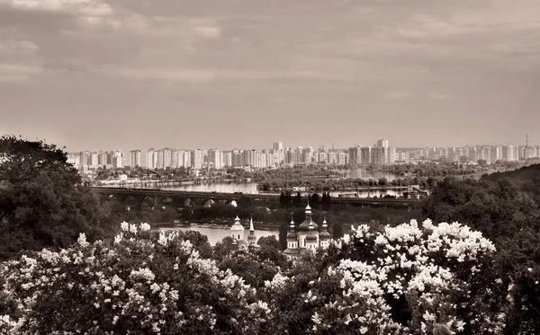 The Orthodox Church on the background of the river and the city, in the garden of blooming lilacs, Kiev, Ukraine (black and white photo)