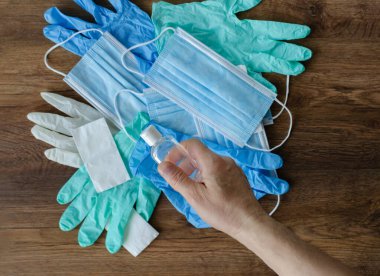 Erkeklerin elindeki dezenfektan tıbbi maskelerin arka planında ve eldivenlerin silgisinde. Tahta bir arka planda COVID-19 'a karşı koruma.