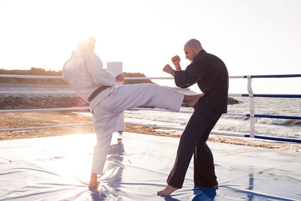 İki profesyonel erkek karate savaşçıları beach boks halka üzerinde mücadele ediyoruz 