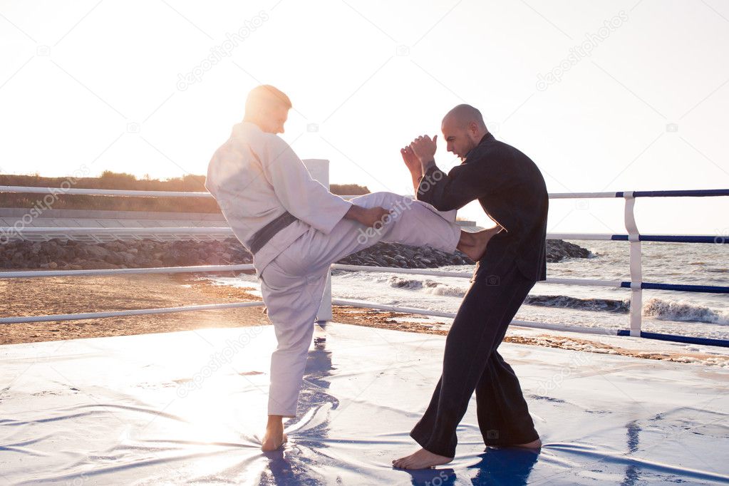 Two professional  karate fighters are fighting on the beach boxing ring 