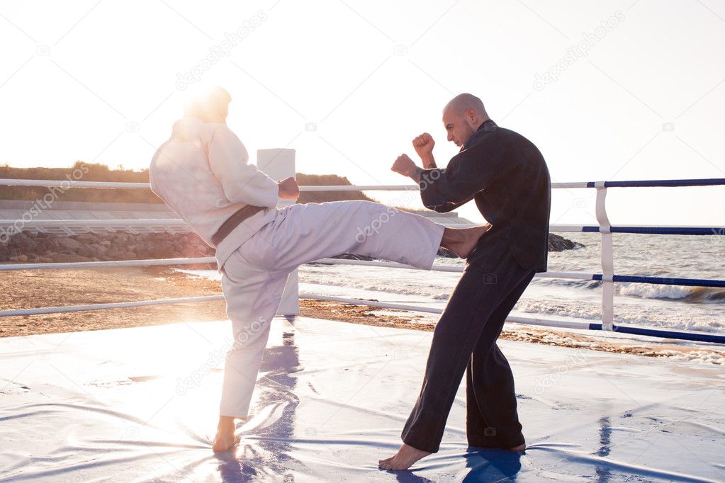 Two professional male karate fighters are fighting on the beach boxing ring 