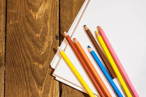 Carta bianca e matite colorate su vecchio tavolo di legno — Foto Stock