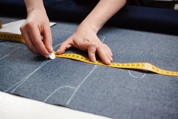 Tangan penjahit memotong kain jeans dengan pola gunting dan mengukur pita di atas meja putih — Stok Foto