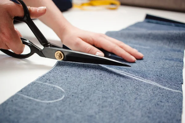 Hands of seamstress cutting a jeans fabric with scissors on white table — Stock Photo, Image