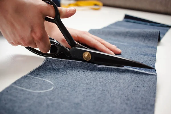 Handen van naaister een jeans stof knippen met een schaar op witte tafel — Stockfoto