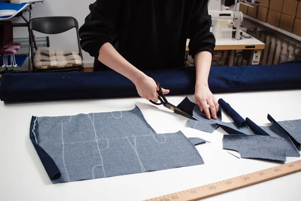 Hands of seamstress cutting a jeans fabric with scissors on white table — Stock Photo, Image