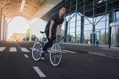  genç adam şehirde sokak bisiklet sürme. Adam beyaz tekerlekli, büyük ayna windows arka plan mavi bisiklet üzerinde