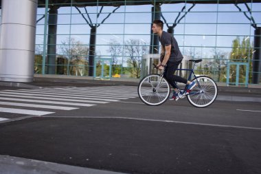  genç adam şehirde sokak bisiklet sürme. Adam beyaz tekerlekli, büyük ayna windows arka plan mavi bisiklet üzerinde