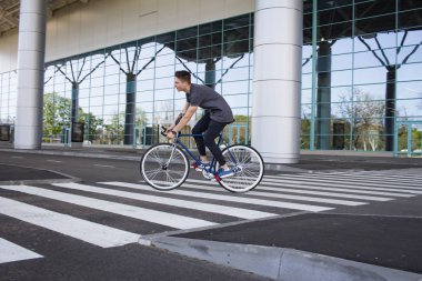  genç adam şehirde sokak bisiklet sürme. Adam beyaz tekerlekli, büyük ayna windows arka plan mavi bisiklet üzerinde