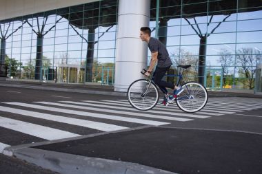  genç adam şehirde sokak bisiklet sürme. Adam beyaz tekerlekli, büyük ayna windows arka plan mavi bisiklet üzerinde