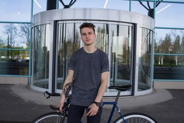 Dükkanı pencere arka plan üzerinde gri gömlek duran adam. genç bir adamın yanında mavi Bisiklet. 