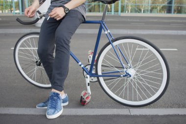 Onun mavi bisiklet üzerinde oturan adam resmini kapatın. Adam siyah kot ve mavi ayakkabılar bacaklar beyaz tekerlekli mavi retro sabit vites bisiklet oturmak 