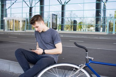 cep telefonu, caddenin üzerinde sabit vites bisiklet üzerinde genç hipster manifatura. büyük ayna windows arka plan 