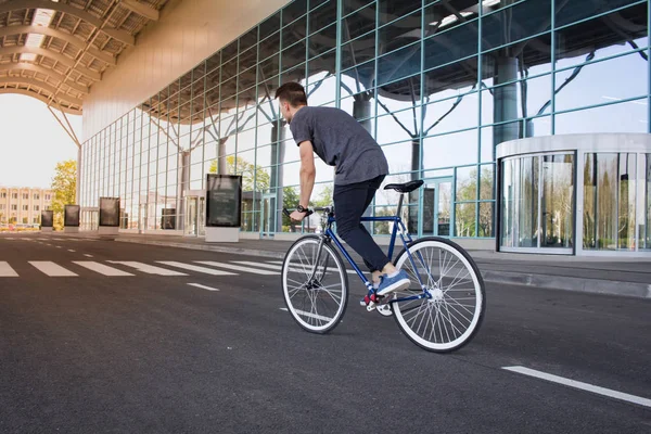 젊은이 도시 거리에 자전거를 타고입니다. 백색 바퀴, 큰 거울 윈도우 배경으로 파란 자전거에 남자 — 스톡 사진
