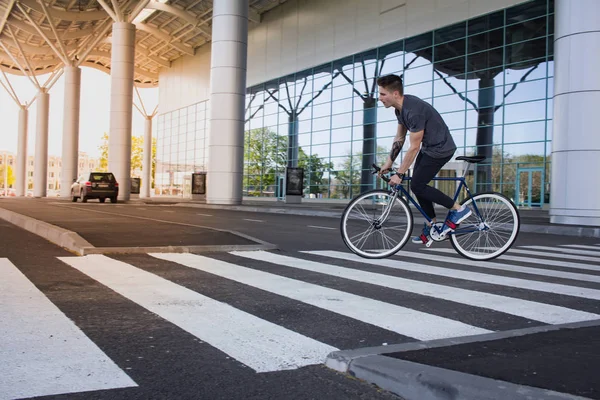 Jonge man rijden op de fiets in de stad straat. Man op blauwe fiets met witte wielen, grote spiegel windows achtergrond — Stockfoto