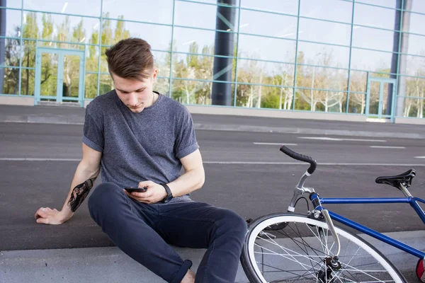 핸드폰, 도시 거리에 고정된 기어 자전거에 젊은 hipster 문자 메시지. 큰 거울 윈도우 배경 — 스톡 사진