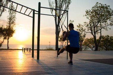 egzersiz süspansiyon ile açık spor salonunda, güçlü adam park, gündoğumu veya günbatımı deniz arka planda sabah erken eğitim kayışlar 