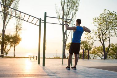 egzersiz süspansiyon ile açık spor salonunda, güçlü adam park, gündoğumu veya günbatımı deniz arka planda sabah erken eğitim kayışlar 