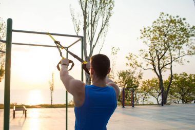 egzersiz süspansiyon ile açık spor salonunda, güçlü adam park, gündoğumu veya günbatımı deniz arka planda sabah erken eğitim kayışlar 