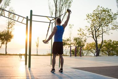 egzersiz süspansiyon ile açık spor salonunda, güçlü adam park, gündoğumu veya günbatımı deniz arka planda sabah erken eğitim kayışlar 