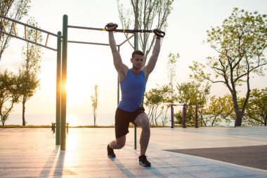 egzersiz süspansiyon ile açık spor salonunda, güçlü adam park, gündoğumu veya günbatımı deniz arka planda sabah erken eğitim kayışlar 