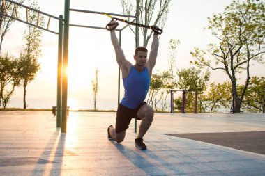 egzersiz süspansiyon ile açık spor salonunda, güçlü adam park, gündoğumu veya günbatımı deniz arka planda sabah erken eğitim kayışlar 