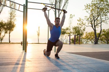 egzersiz süspansiyon ile açık spor salonunda, güçlü adam park, gündoğumu veya günbatımı deniz arka planda sabah erken eğitim kayışlar 