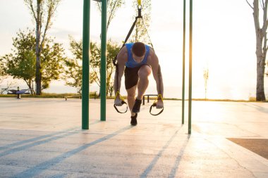 egzersiz süspansiyon ile açık spor salonunda, güçlü adam park, gündoğumu veya günbatımı deniz arka planda sabah erken eğitim kayışlar 