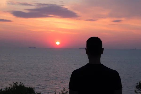 Silhouette eines fitten jungen Mannes, der den Sonnenuntergang oder -aufgang im Meer oder Ozean beobachtet — Stockfoto