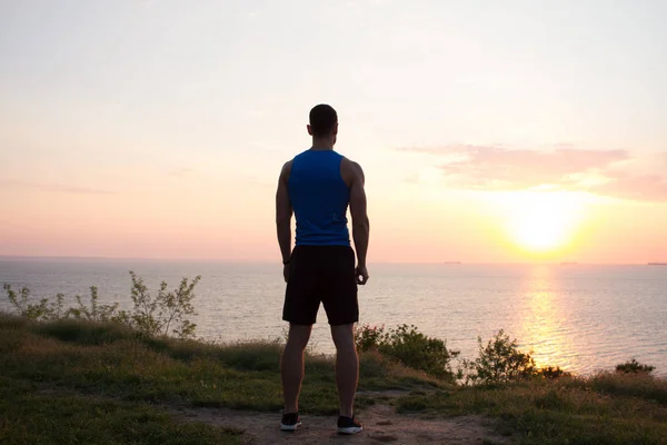 Dopasowanie runner oglądanie wschodu lub zachodu słońca z noszenia pięści, młodego sportowca na trawie podczas wschodu słońca na morzu — Zdjęcie stockowe