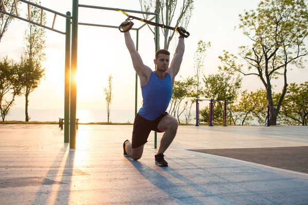 Egzersiz süspansiyon ile açık spor salonunda, güçlü adam park, gündoğumu veya günbatımı deniz arka planda sabah erken eğitim kayışlar — Stok fotoğraf