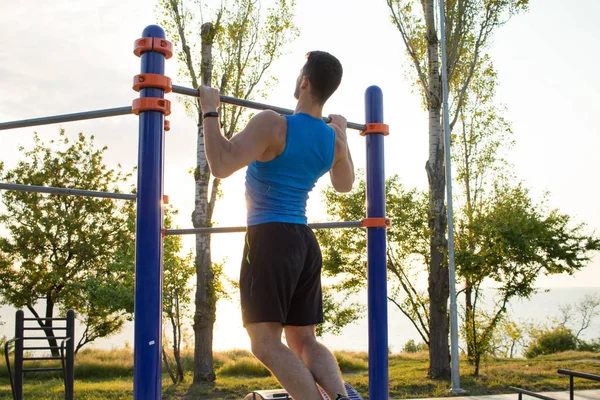 Musclé homme faisant pull-ups sur barre horizontale, la formation de l'homme fort sur la salle de gym de parc en plein air le matin . — Photo