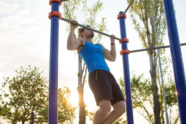 Musclé homme faisant pull-ups sur barre horizontale, la formation de l'homme fort sur la salle de gym de parc en plein air le matin . — Photo
