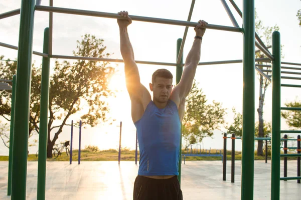 Musclé homme faisant pull-ups sur barre horizontale, la formation de l'homme fort sur la salle de gym de parc en plein air le matin . — Photo