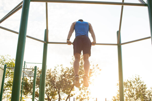 Muscular man doing pull-ups on horizontal bar, training of strongman on  outdoor park gym in the morning. 