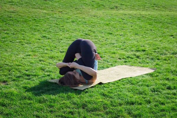 Giovane bella donna in forma facendo asans yoga sull'erba verde con tappetino yoga — Foto Stock