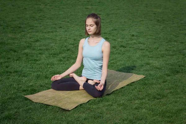 Joven hermosa mujer en forma haciendo yoga asans en la hierba verde con estera de yoga — Foto de Stock