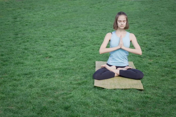 Mooie jonge past vrouw doeing yoga asans op het groene gras met yoga mat — Gratis stockfoto