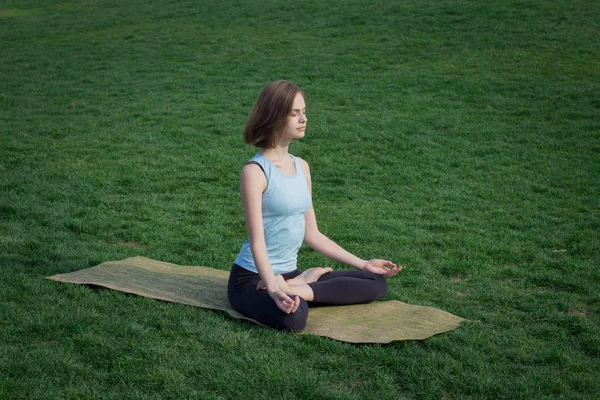 Joven hermosa mujer en forma haciendo yoga asans en la hierba verde con estera de yoga — Foto de Stock