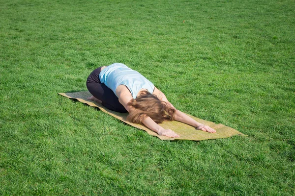 Giovane bella donna in forma facendo asans yoga sull'erba verde con tappetino yoga — Foto Stock