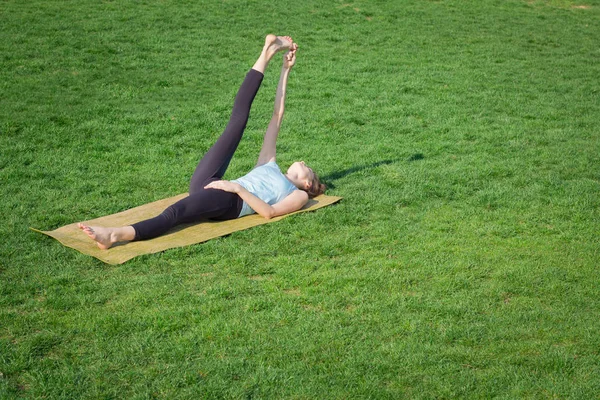 Młody piękny pasuje Asanami joga kobieta doeing na zielonej trawie z matę do jogi — Zdjęcie stockowe