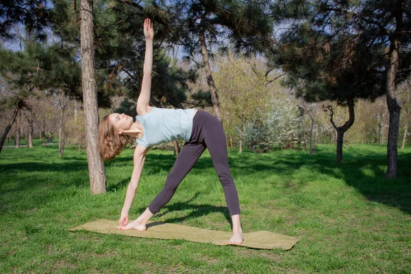 Mujer joven haciendo ejercicios de yoga en el parque de verano de la ciudad . — Foto de Stock